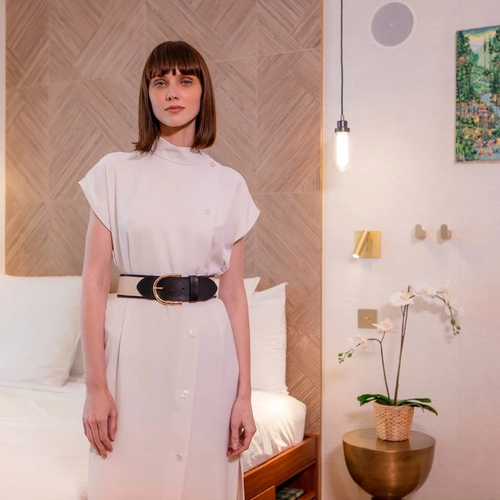 La modelo en el dormitorio, entre texturas de madera, ropa de cama clara y detalles dorados.