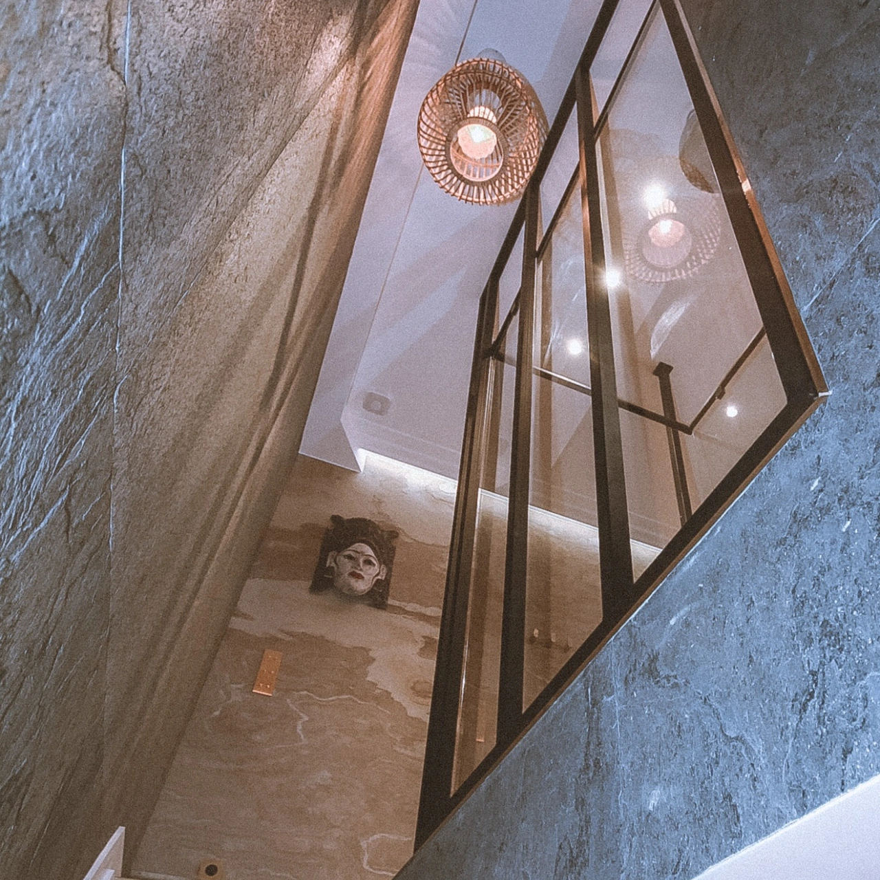 Duplex staircase framed by natural stone veneers and a glass partition