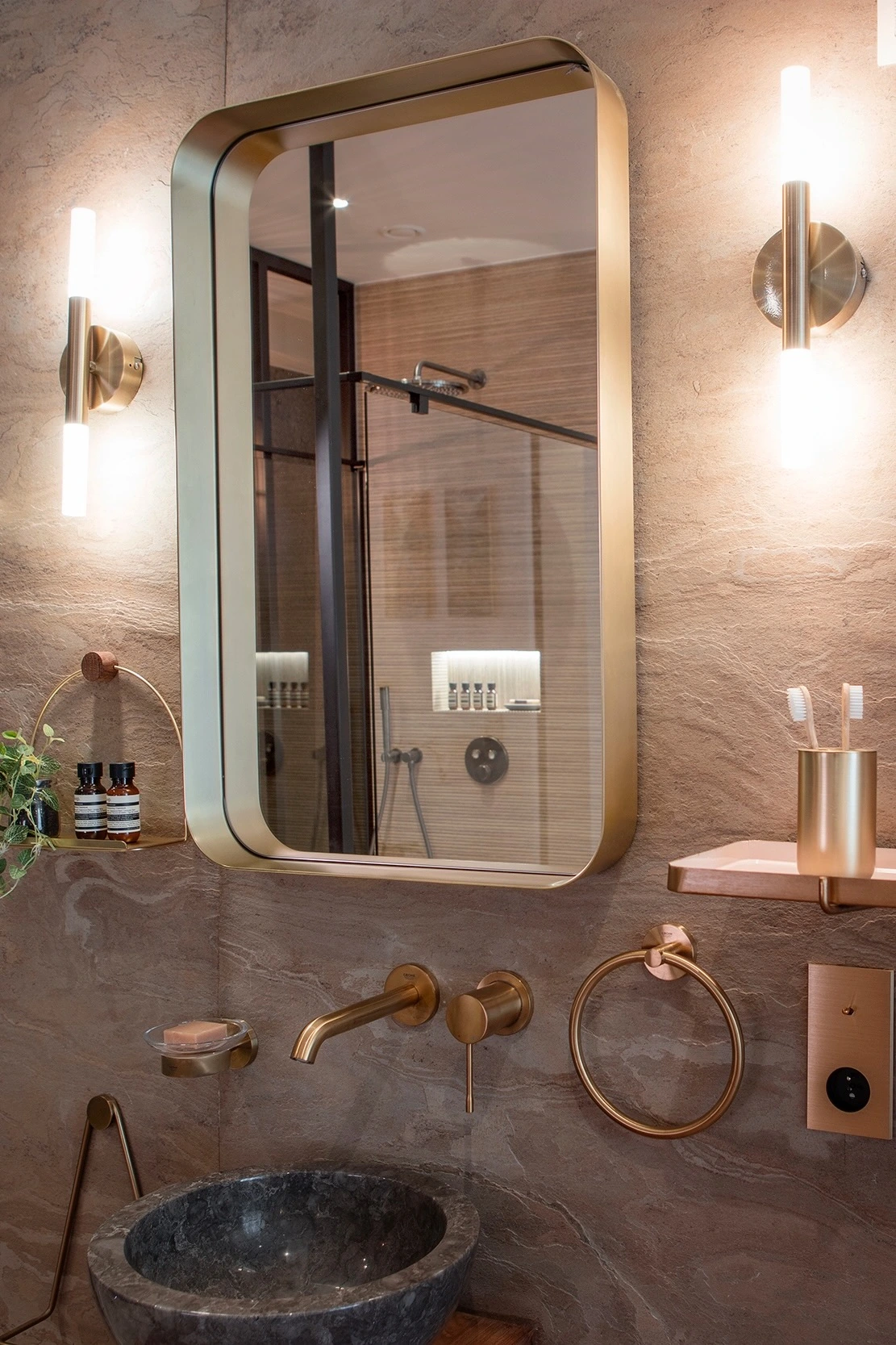 Miroir doré et vasque en pierre, avec la douche visible dans le reflet