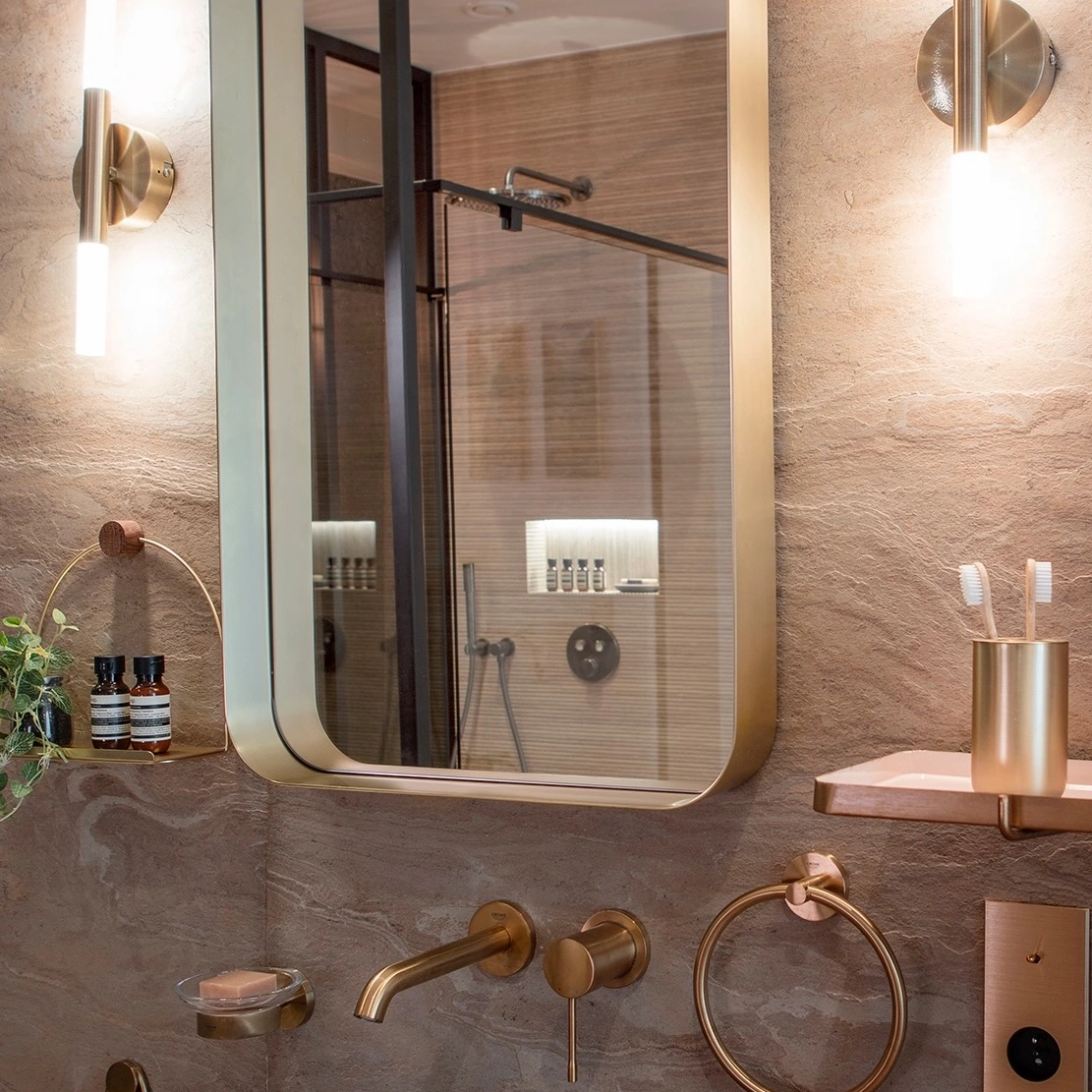 Golden mirror and stone basin, with the shower visible in the reflection